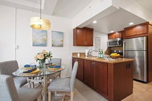 Eine moderne Küche mit Holzschränken, Edelstahlgeräten und einem Essbereich mit Glastisch und Stühlen.