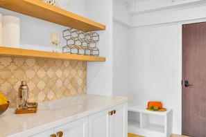 Eine Küche mit weißen Schränken, einer Marmorarbeitsplatte, einem Holzregal und einer ornamentierten Spritzschutzleiste.