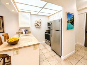 A kitchen with a central island, stainless steel appliances, a microwave, and a framed picture on the wall. - Whaler | Ocean View 3 BR Sleeps 12 | Car Incl. w/ 6+ Nights | ML-4229 by KBM (Lahaina)