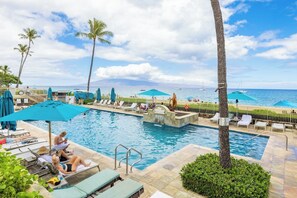 A pool area with lounge chairs, umbrellas, and a view of the ocean. - Whaler | Ocean View 3 BR Sleeps 12 | Car Incl. w/ 6+ Nights | ML-4229 by KBM (Lahaina)