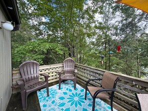 Un terraço de fusta amb un estenedora blau estampat, dues cadiretes Adirondack i una tanca de fusta.