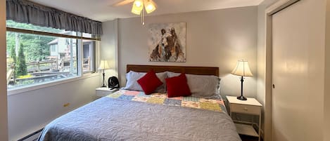 Une chambre à coucher avec un lit, deux tables de chevet avec des lampes, un ventilateur de plafond, une fenêtre avec des rideaux et un tableau accroché au mur.