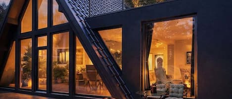 Un edificio moderno con techo inclinado y amplias ventanas, una chimenea esférica y una zona de estar con vistas al interior.