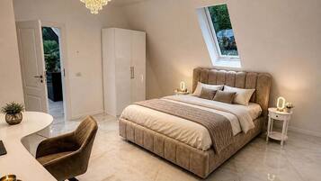 A bedroom with a large bed, a desk, a chair, and a chandelier.