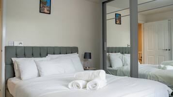 A hotel room with a bed, a nightstand, a lamp, a mirror, and a door.