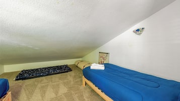 A small, single-bed room with a blue mattress, a wooden frame, a beige carpet, and a small blue chair.
