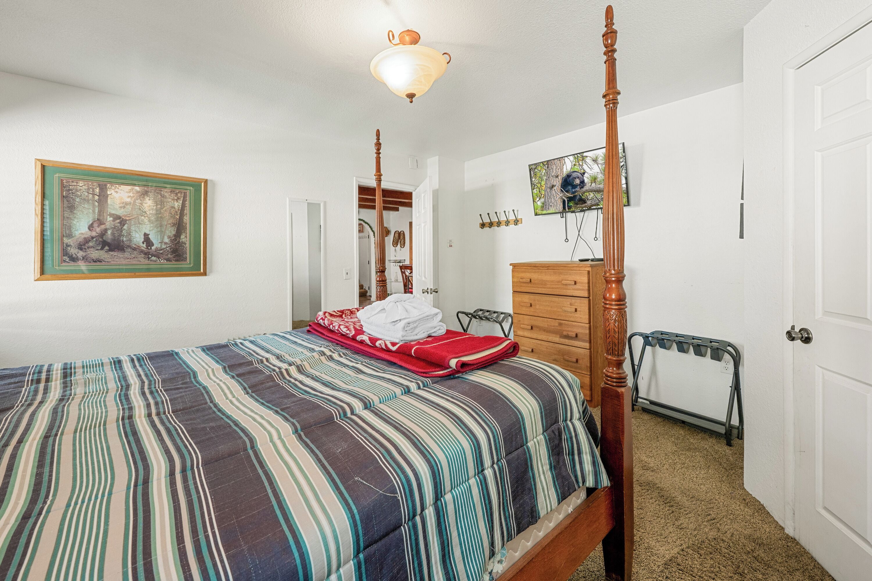 A bedroom with a four-poster bed, a dresser, a television, and a painting on the wall.