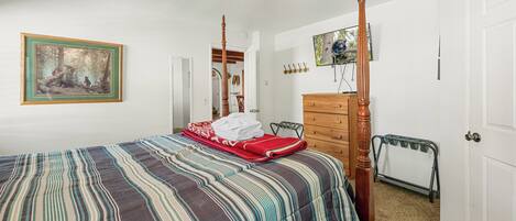 A bedroom with a four-poster bed, a dresser, a television, and a painting on the wall.
