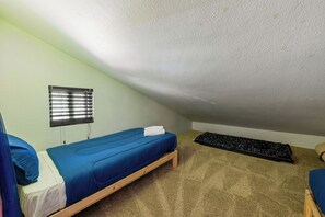 Una habitación pequeña individual con una cama individual superpuesta, una ventana con persianas, piso alfombrado y un tapete negro en el suelo.