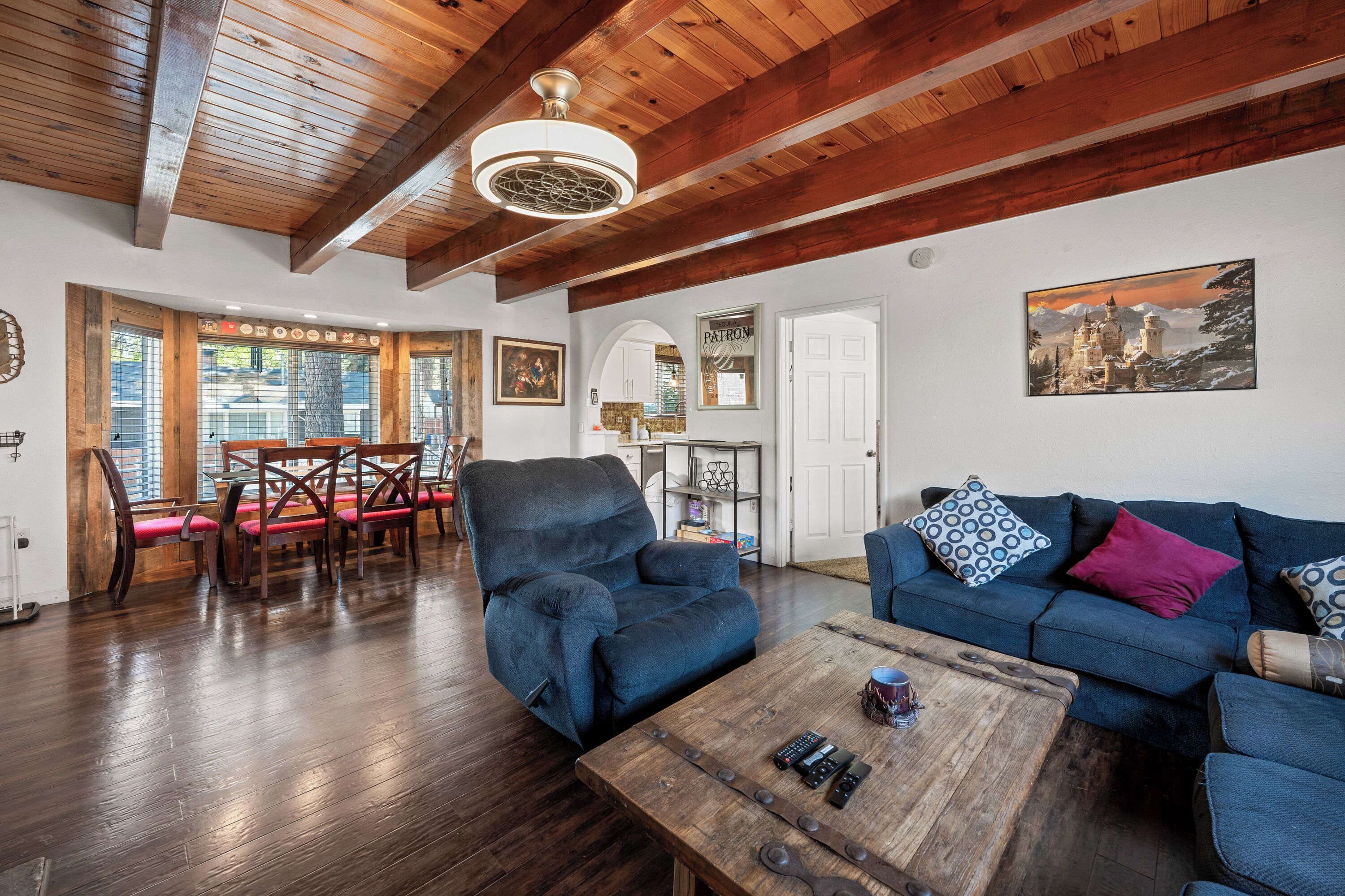 Ein geräumiges Wohnzimmer mit Holzbalkendecke, einem blauen Sofa, einem Couchtisch und einem Essbereich mit Holzsesseln.