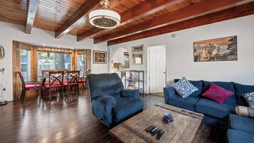 A spacious living room with a wooden ceiling, a blue sofa, a coffee table, and a dining area with wooden chairs.
