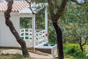 Una cabaña de madera con un porche blanco y un jacuzzi.