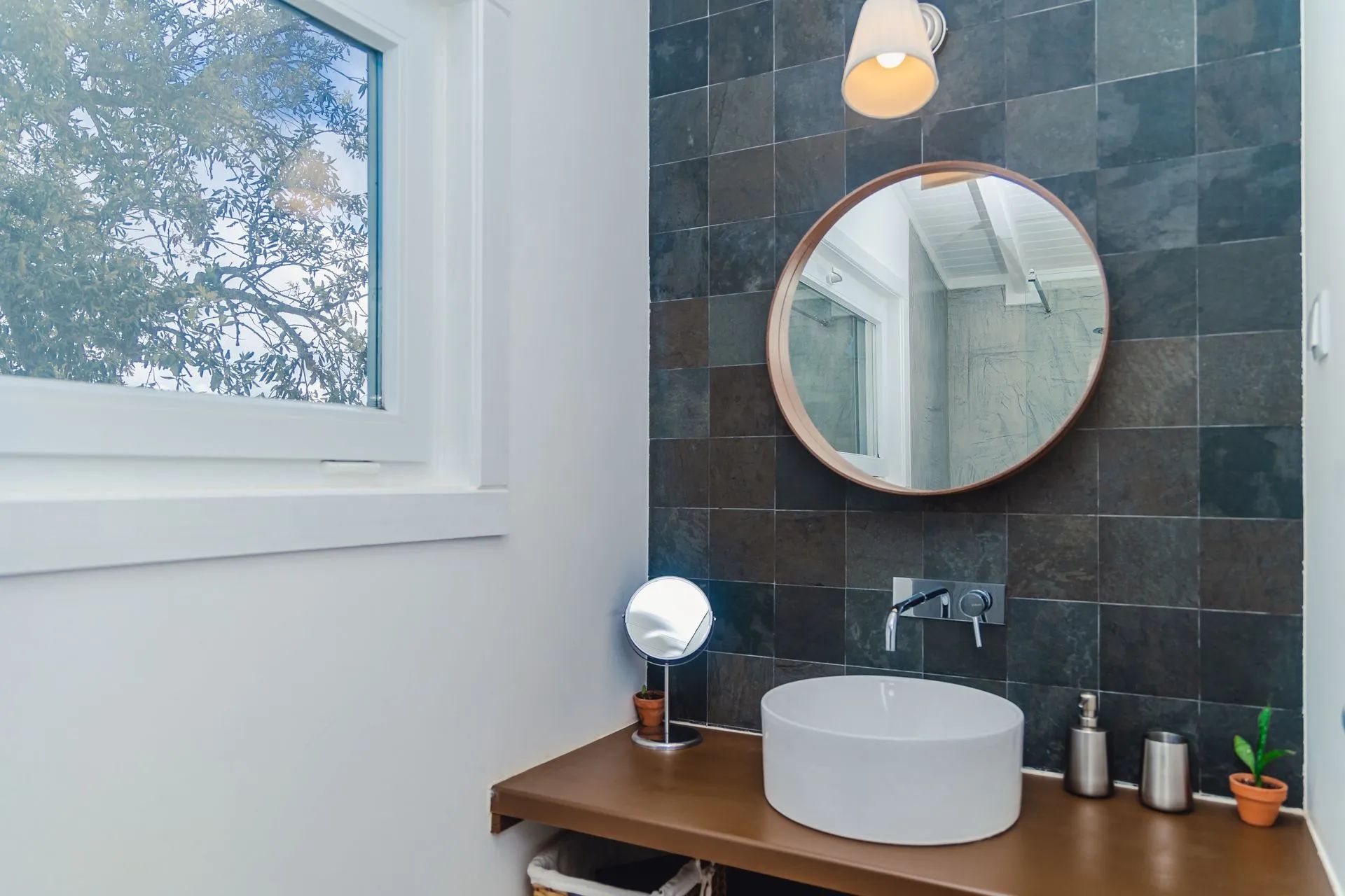 Un baño con un espejo redondo, un lavamanos blanco y una ventana.
