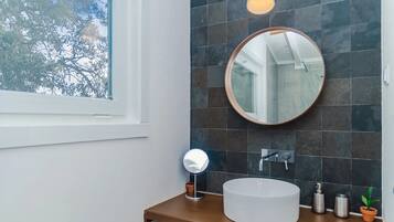 Un baño con un espejo redondo, un lavamanos blanco y una ventana.