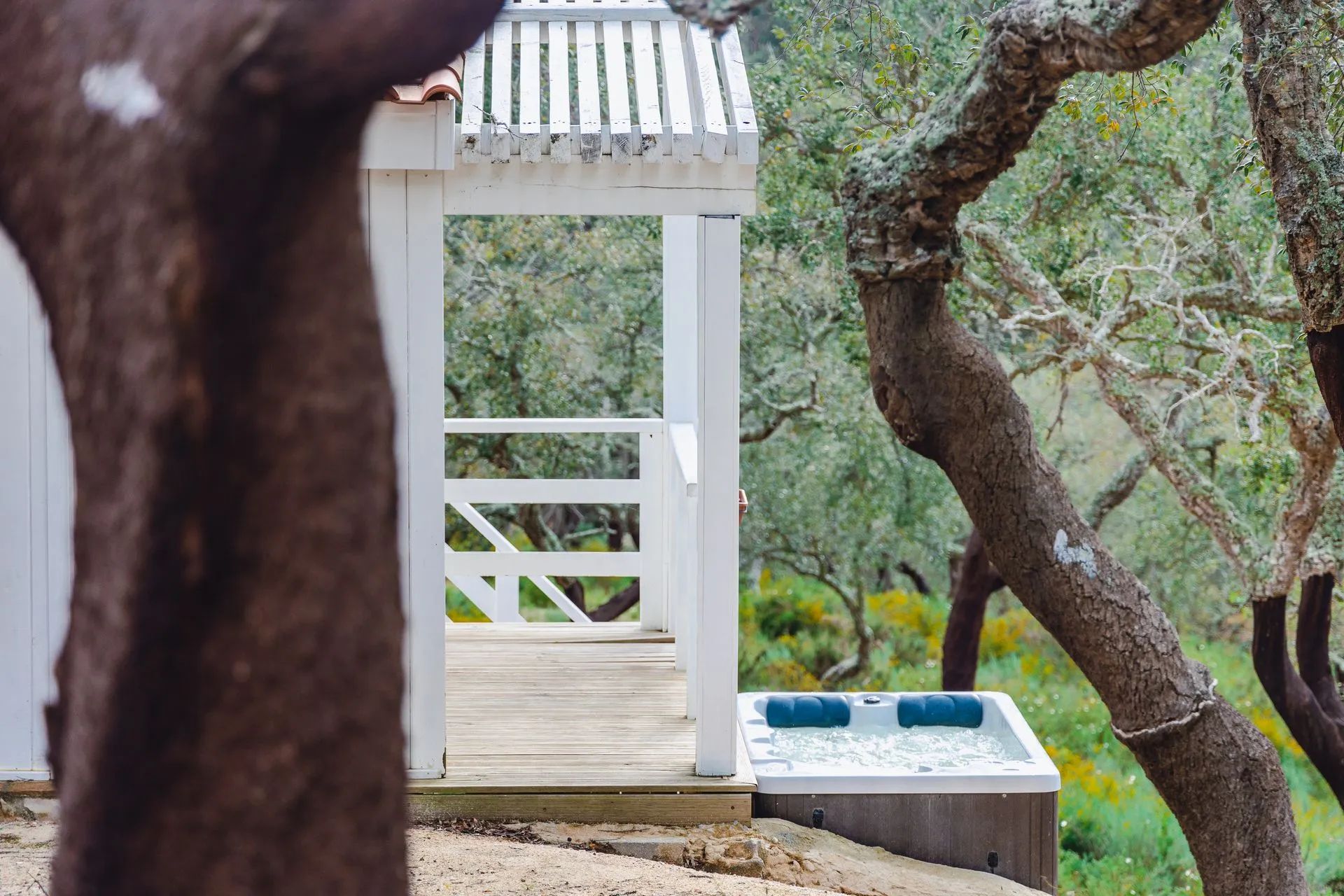 Eine Holzterrasse führt zu einem weißen Gazebo mit Whirlpool und Wasserspiel.