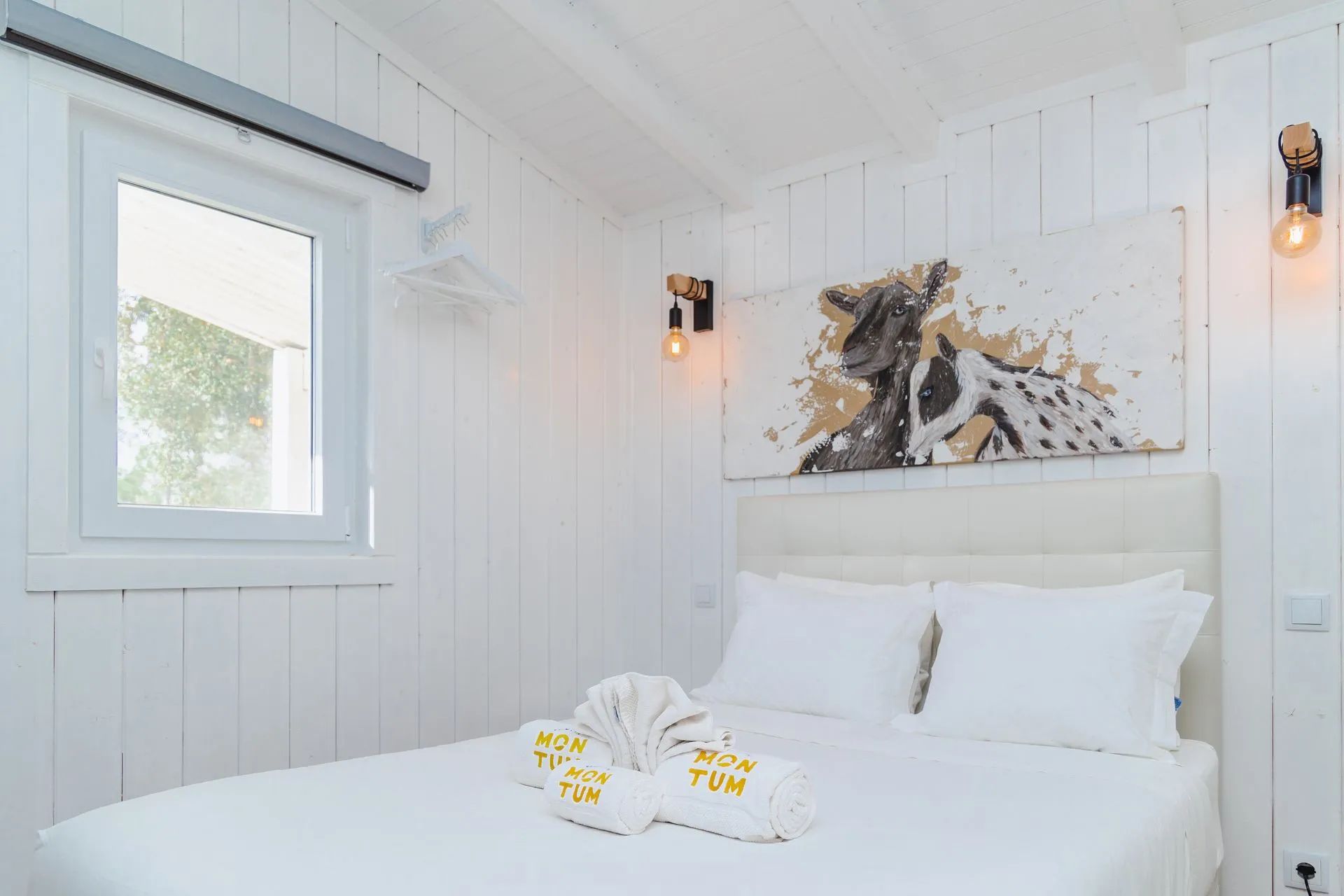 Una habitación de hotel con una cama, una ventana y un cuadro colgado en la pared.