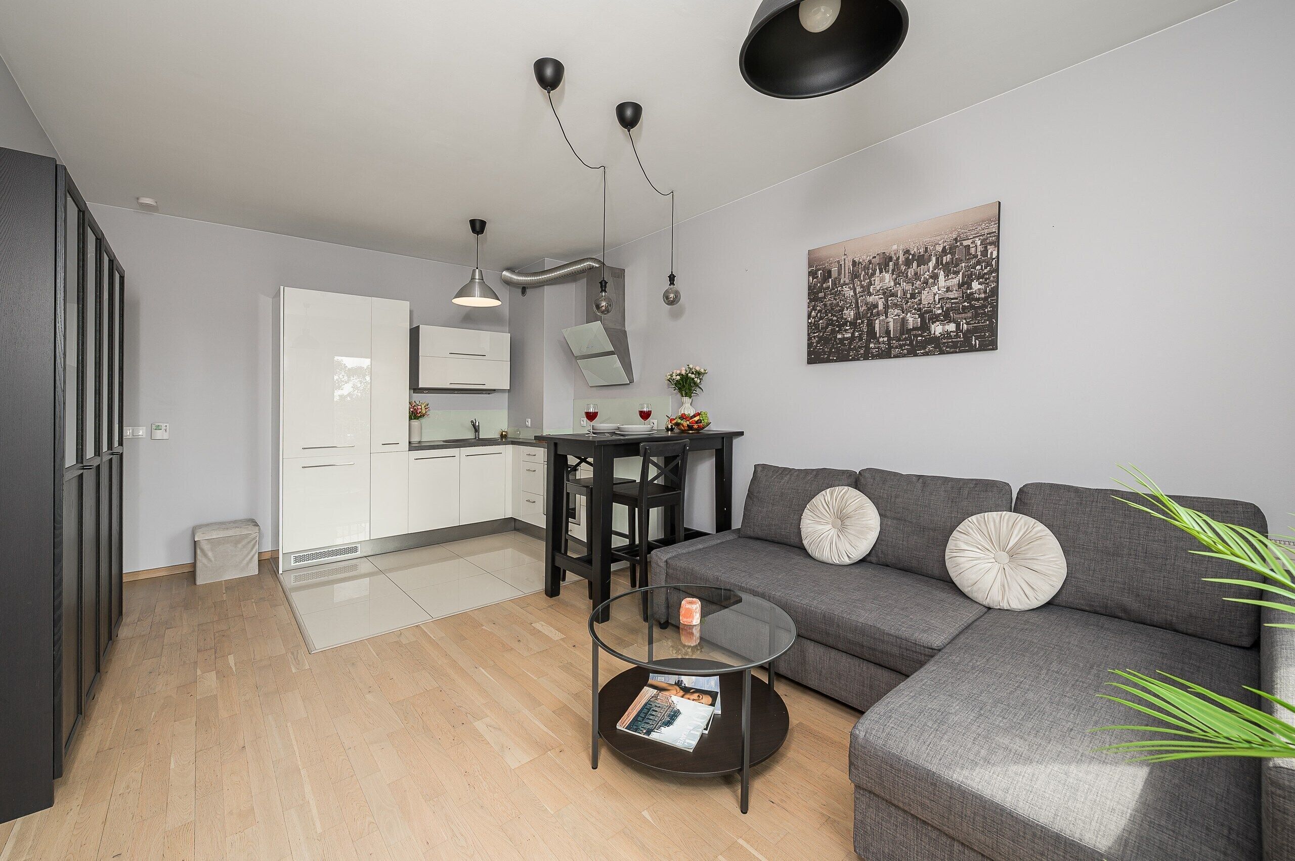 Un espace de vie moderne comprenant un canapé gris, une table à manger et un coin cuisine.