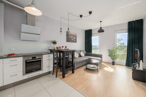 Een moderne keuken met een Bosch oven, een eettafel met stoelen, een grijze bank en een groot raam met gordijnen.