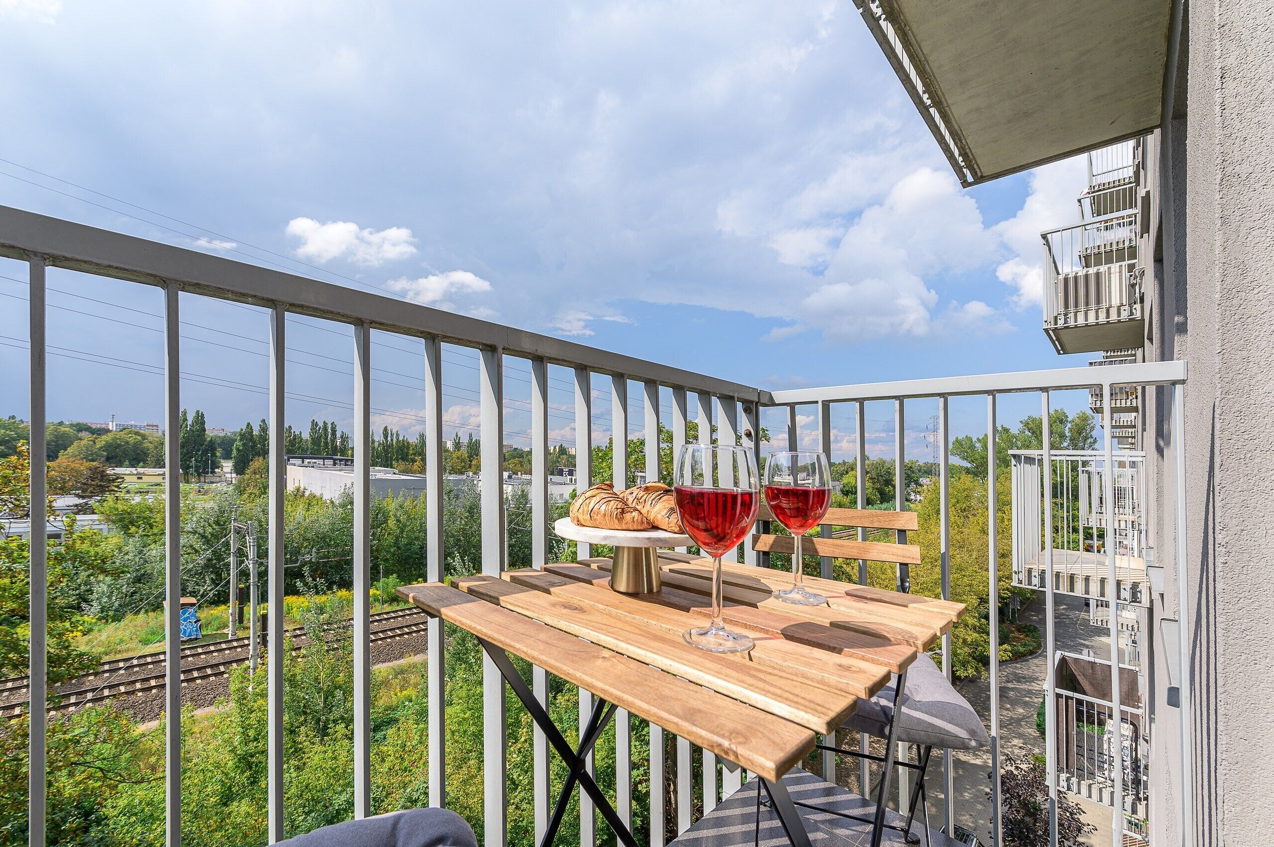 A balcony with a wooden table, two wine glasses, and a loaf of bread.