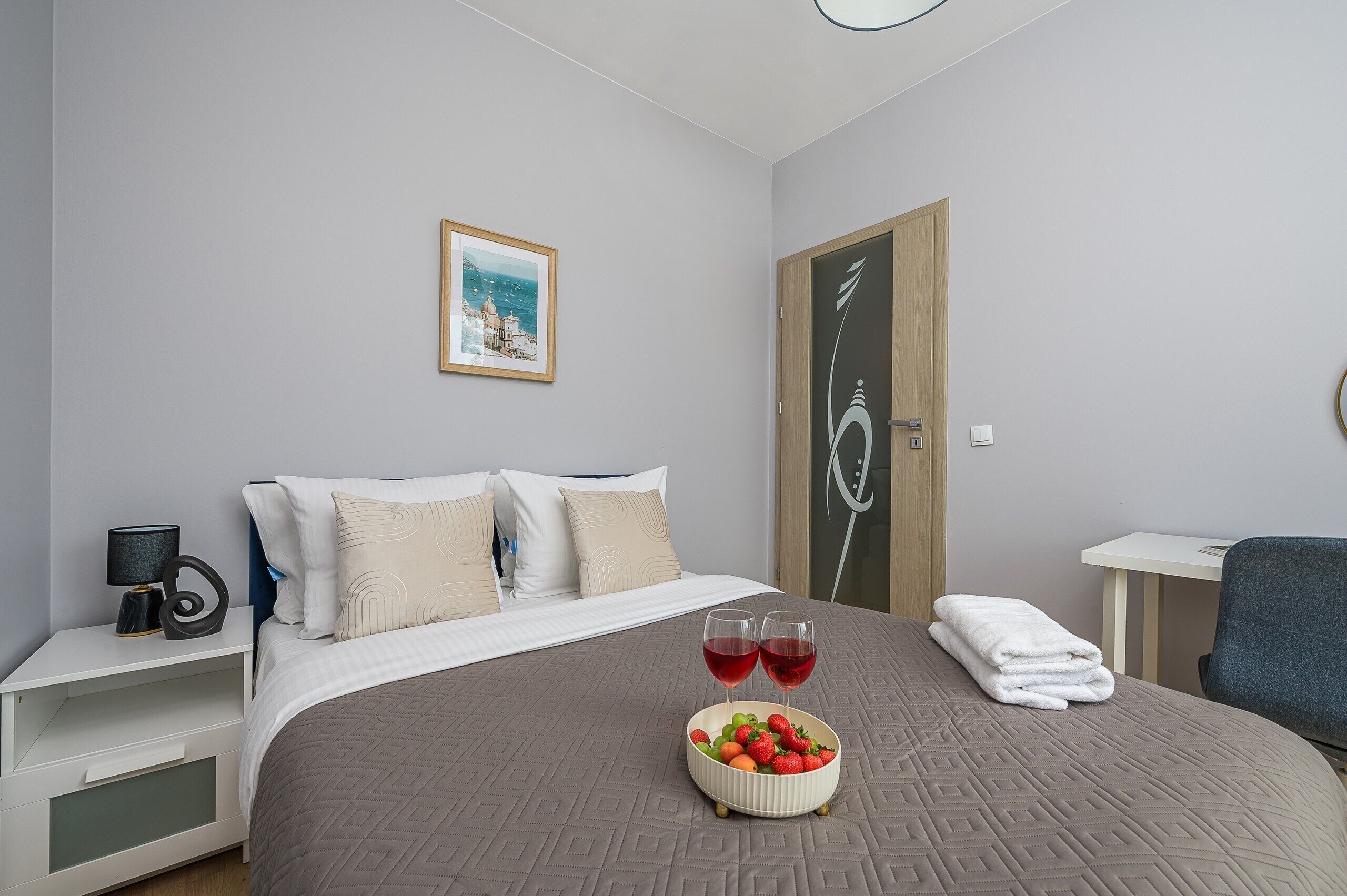 Ett hotellrum med en säng, ett sängbord med en lampa, en inramad tavla på väggen och en dörr med ett dekorativt mönster.