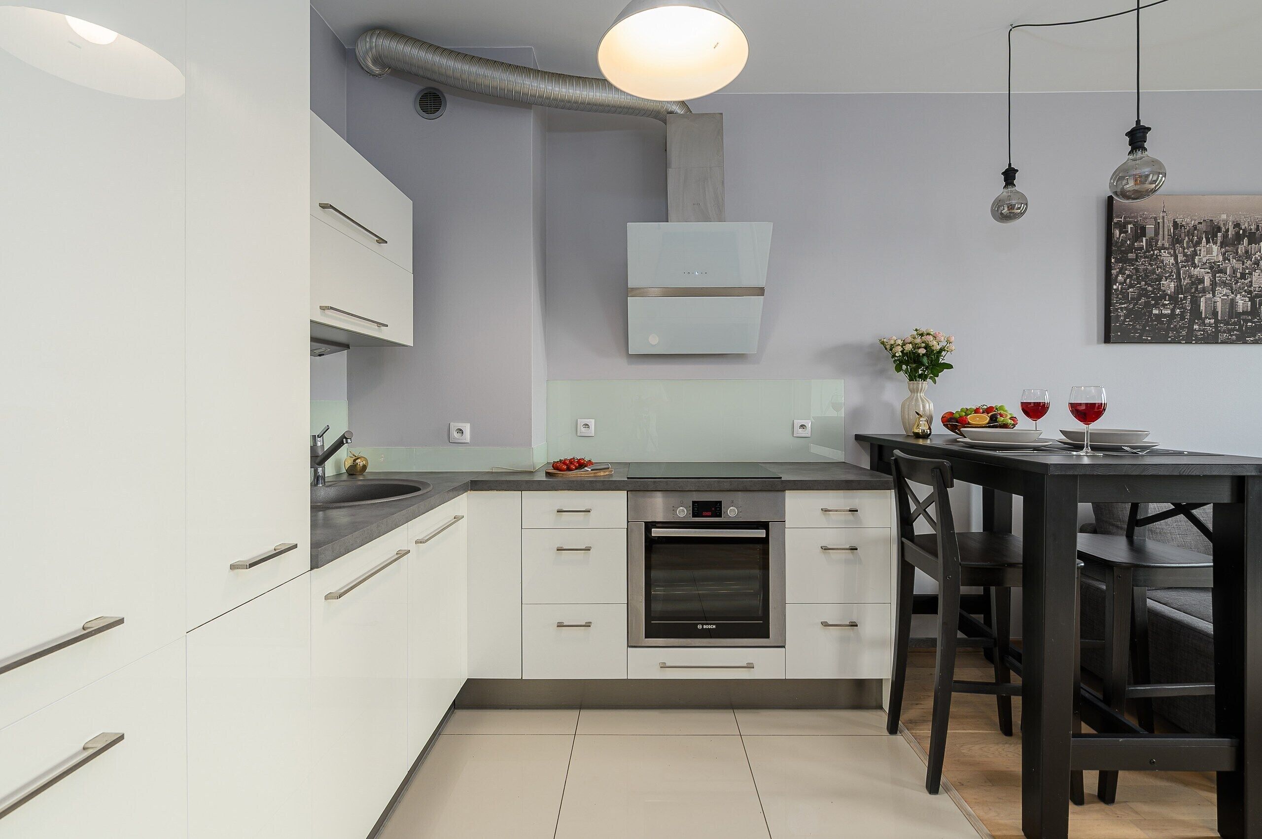 A modern kitchen with white cabinetry, a Bosch oven, and a dining area with a black table and chairs.