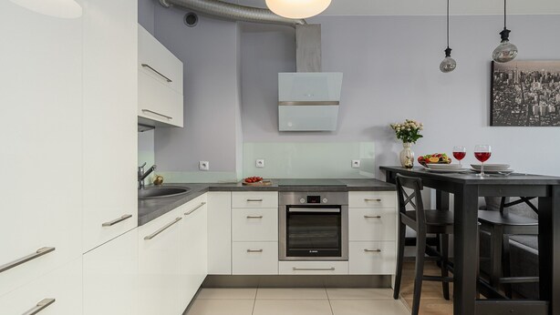 Una cocina moderna con muebles blancos, un horno Bosch y un comedor con mesa y sillas negras.