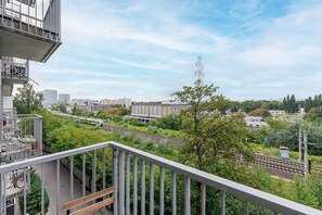 Ein Balkon mit Blick auf Gleise, Grünflächen und entfernte Gebäude.