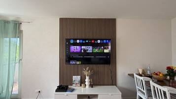 Un salon avec un téléviseur fixé au mur, un meuble de rangement blanc et un coin repas comprenant une table et des chaises.