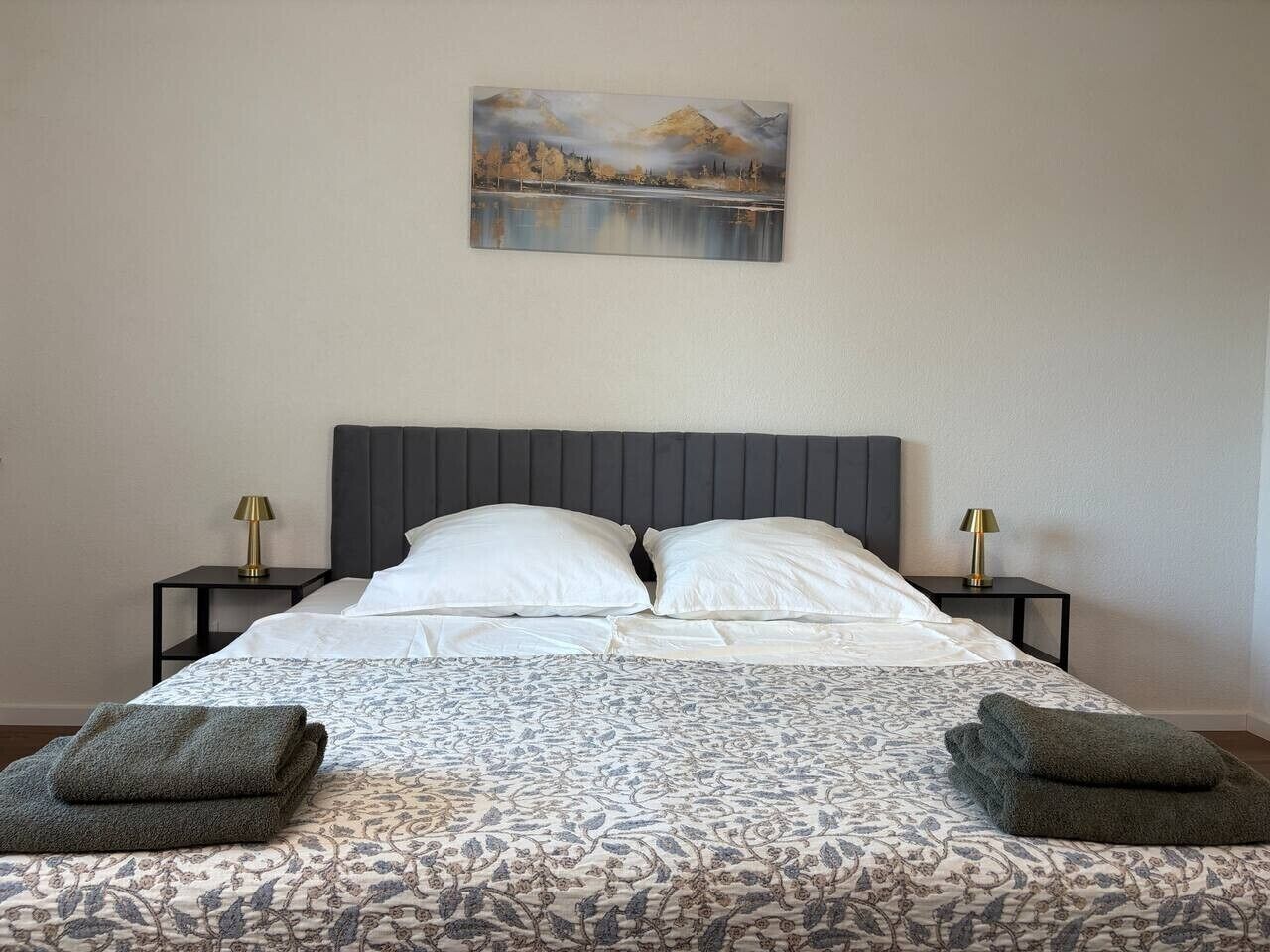 Un lit bien fait, avec une couvre-lit à motifs, deux oreillers et deux tables de chevet dotées de lampes.