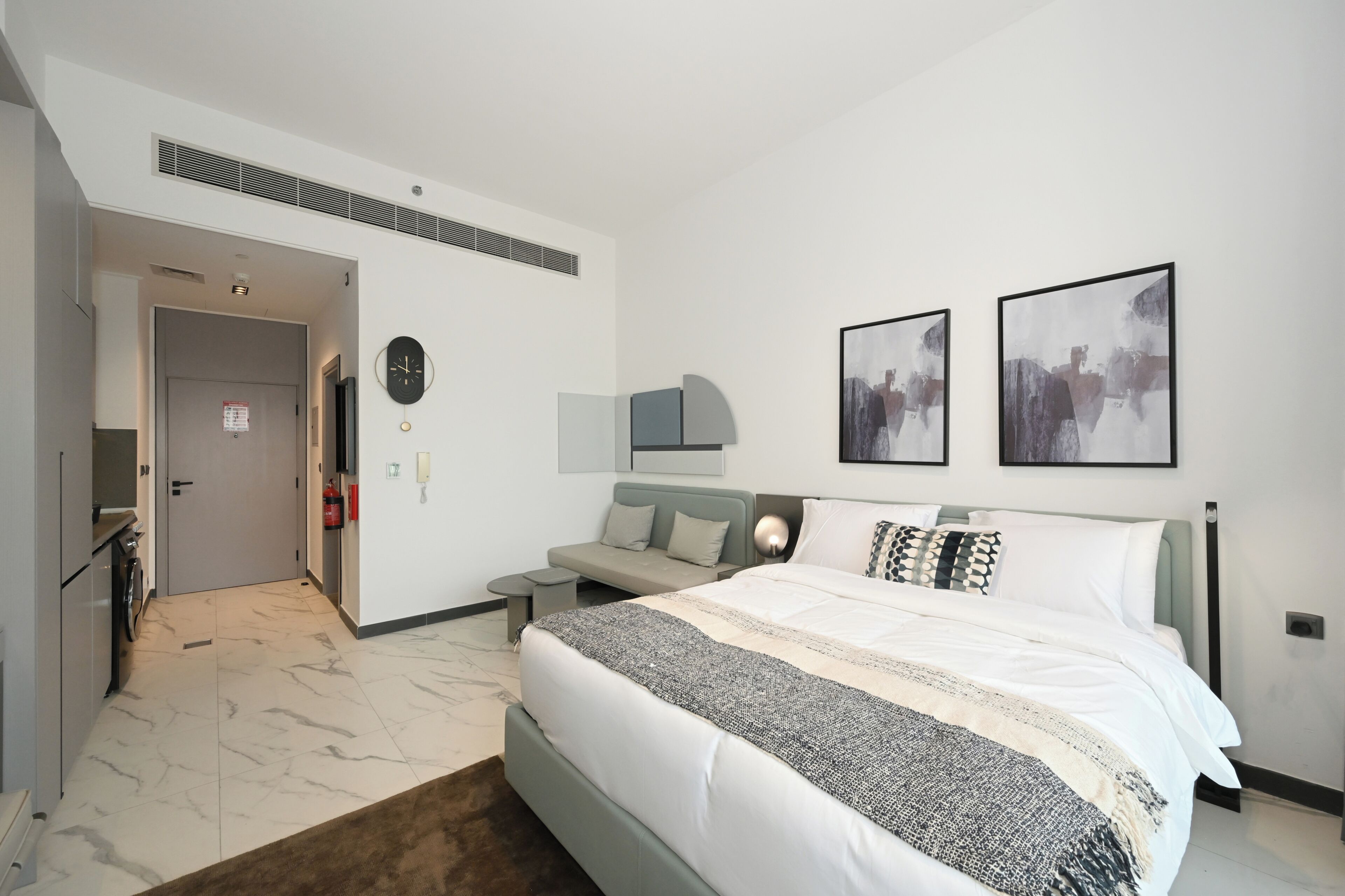 A modern hotel room with a large bed, a sofa, a small table, and two abstract paintings on the wall.