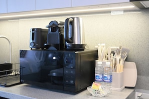 A kitchen with a microwave, a coffee maker, and a kettle on the counter. There are utensils in a holder and two bottles of water. - Bloomfields Studio in Mag Eye 920 (Dubai)