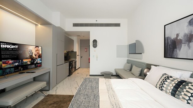 Quarto de hotel moderno com televisão de tela plana, cama, sofá e pequena cozinha.