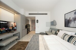 A modern hotel room with a flat-screen TV, a bed, a sofa, and a small kitchen area. - Bloomfields Studio in Mag Eye 920 (Dubai)