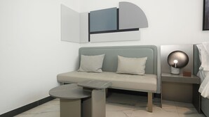 Quarto moderno com sofá cinza, uma mesinha redonda e uma luminária fixada na parede.