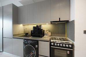 A compact kitchen with a washing machine, a microwave, a gas stove, and a sink. - Bloomfields Studio in Mag Eye 920 (Dubai)
