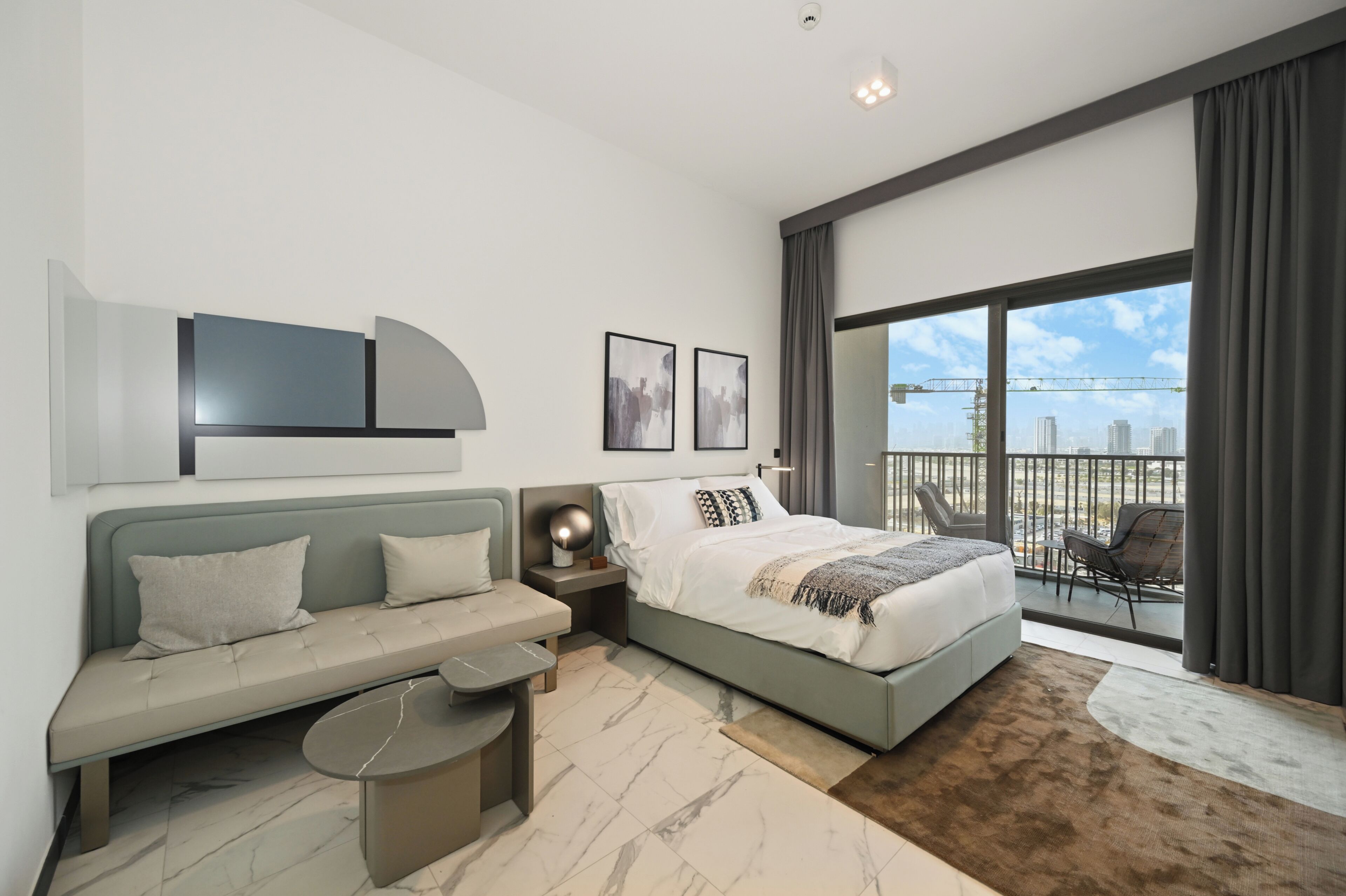 A modern bedroom with a bed, a sofa, a small table, and a balcony with a view.