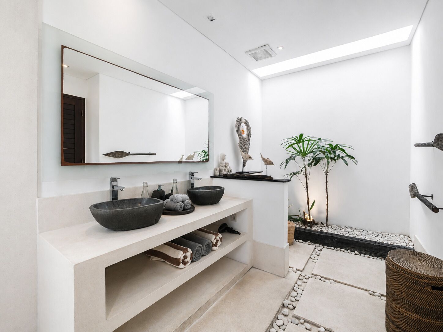 A modern bathroom with a large mirror, two sinks, and a small shelf with towels.