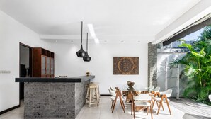 Uma cozinha moderna com uma ilha central, banquetas de madeira e uma mesa de jantar com cadeiras.