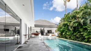 Uma área de piscina moderna com deck de madeira, espreguiçadeiras e um espaço envidraçado.