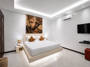 A modern bedroom with a large bed, a flat-screen TV, and a wall-mounted air conditioner. - Villa Saha | Elegant 3BR Pool Oasis Seminyak (Seminyak)