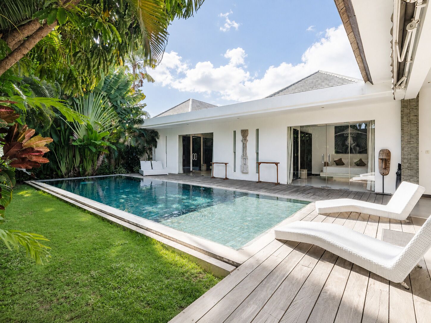 Une maison moderne dotée d’une piscine, d’une terrasse en bois et d’une végétation luxuriante.