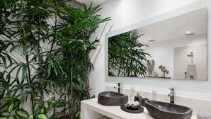 Et stilfuldt badeværelse med et stort spejl, to væghængte håndvaske og mange planter.