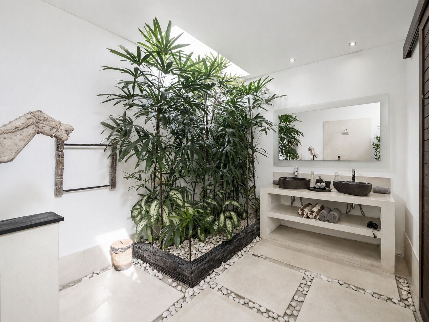 A modern bathroom with a large potted plant, a mirror, and a sink with two basins.