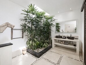 A modern bathroom with a large potted plant, a mirror, and a sink with two basins. - Villa Saha | Elegant 3BR Pool Oasis Seminyak (Seminyak)