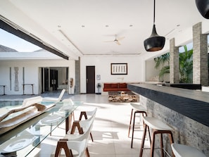 A modern interior with a glass dining table, seating, a ceiling fan, and a view of the outdoors. - Private Tropical Hideaway in Seminyak (Seminyak)