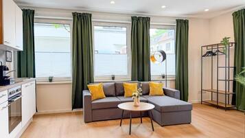 A modern living room with a grey sectional sofa, a round coffee table, and a kitchen area with white cabinets.