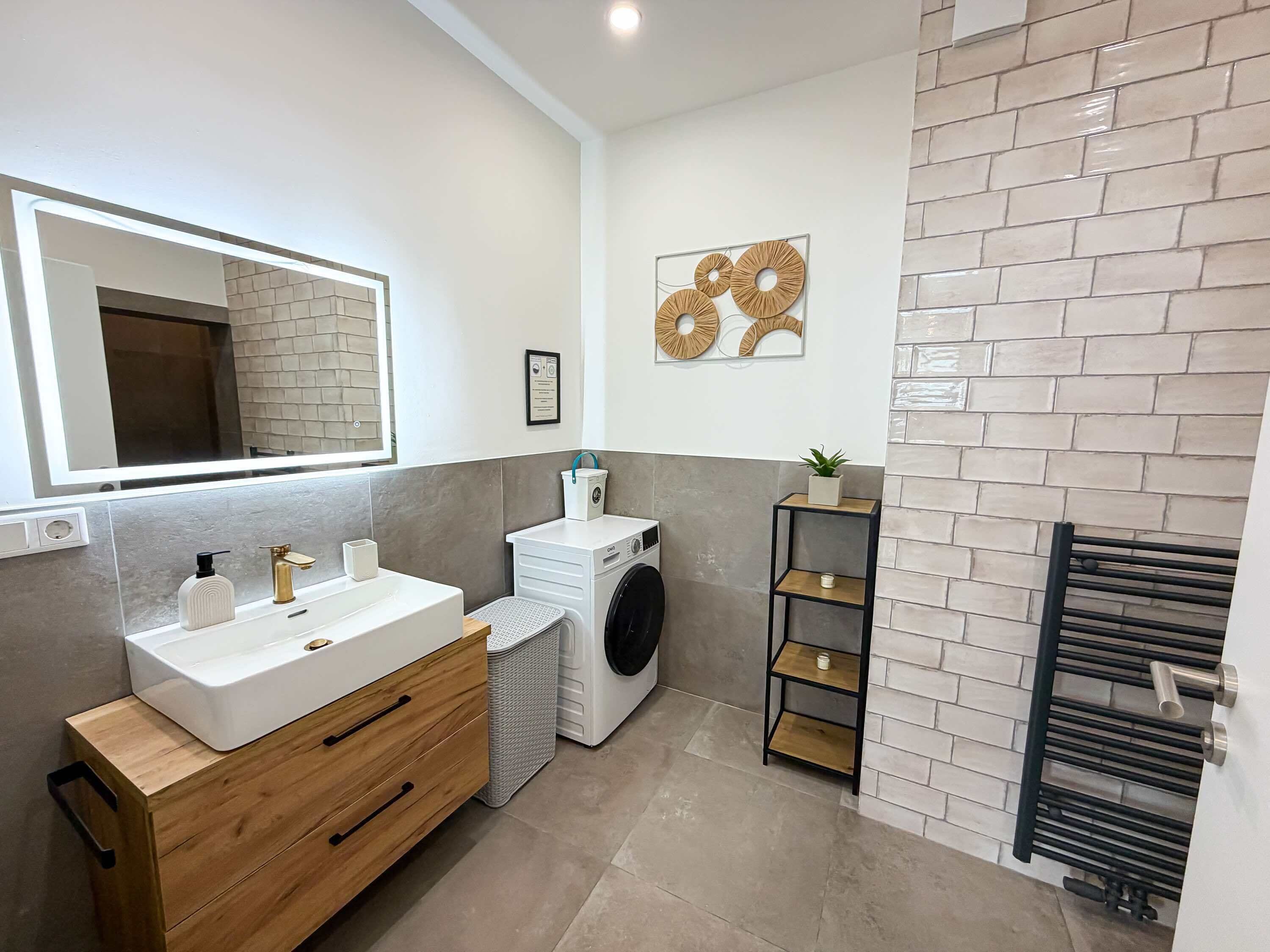 Une salle de bain moderne équipée d’un meuble-lavabo, d’un lave-linge, d’un radiateur et d’œuvres d’art décoratives murales.