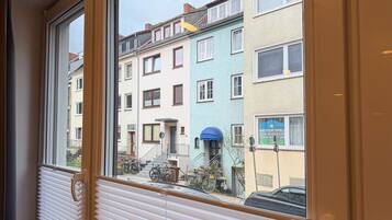 Finestra amb vista a un edifici d'apartaments de diverses plantes i balcons, amb una bicicleta aparcada a l'exterior.