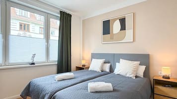 Een hotelkamer met twee bedden, een raam met zonwering, een abstract kunstwerk aan de muur en bedlampjes.