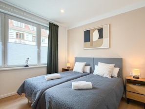 Ein Hotelzimmer mit zwei Betten, einem Fenster mit Jalousien, einem an der Wand hängenden abstrakten Kunstwerk und Nachttischlampen.